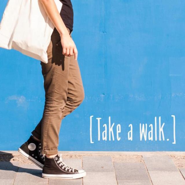 Person in sneakers with a bag walking on a sidewalk against a cheerful blue wall. Text: "Take a walk"