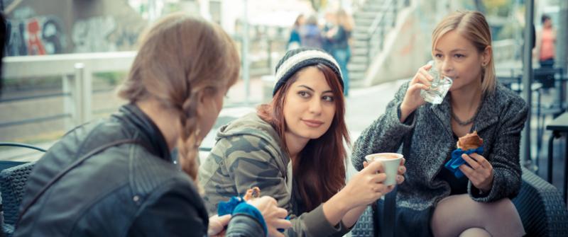 Photo of three women sitting on the patio of a coffeehouse, sipping drinks and eating pastries.