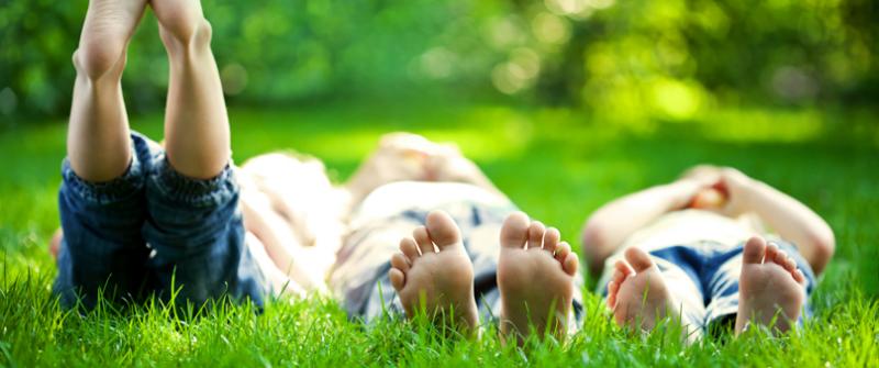 Raise Your Feet Photo of three kids lying barefoot in the grass. Their feet are close to the camera. One kid has his feet raised to the sky.