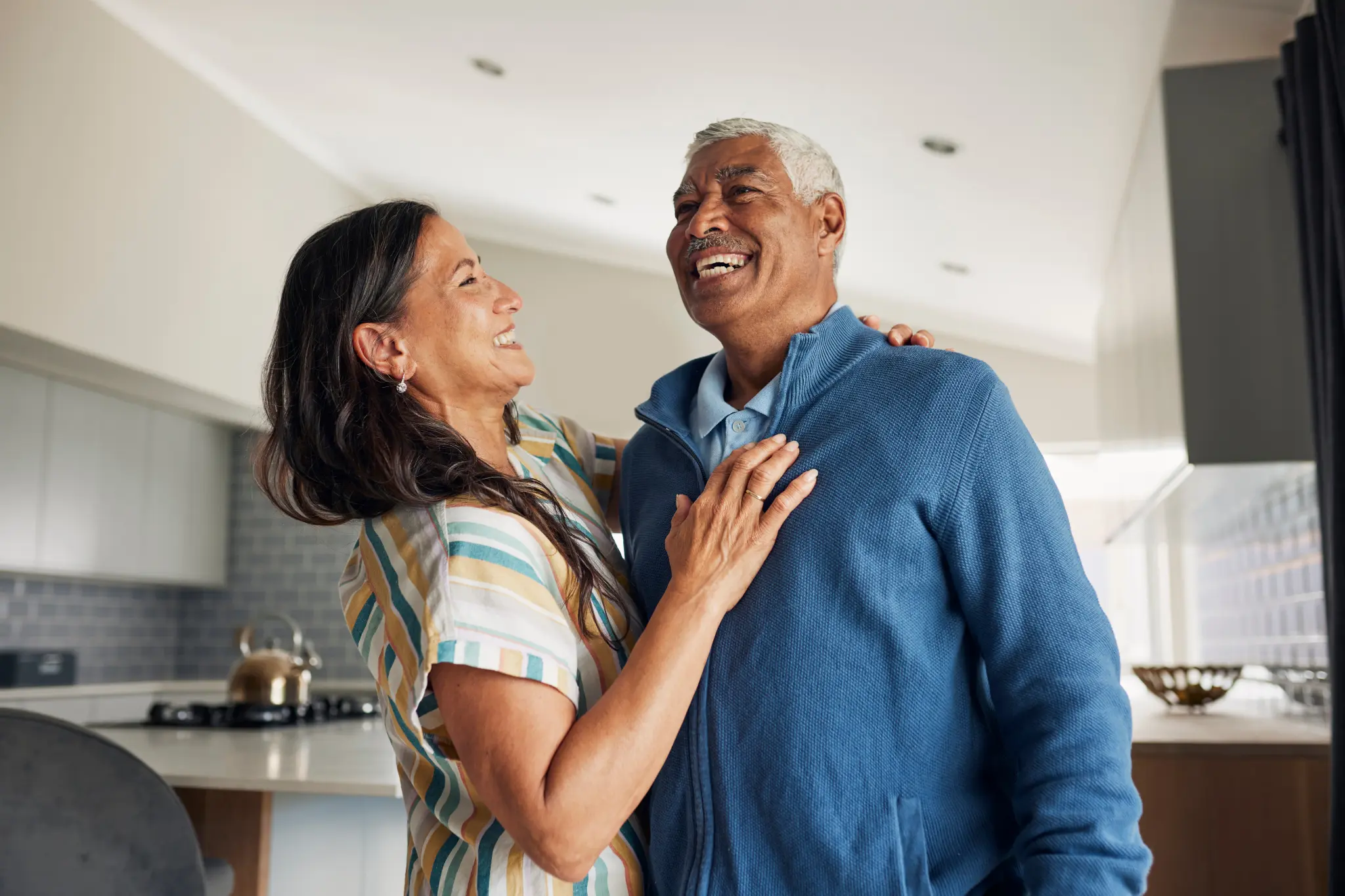 Image of an older couple in a kitchen, smiling and enjoying a celebratory embrace.