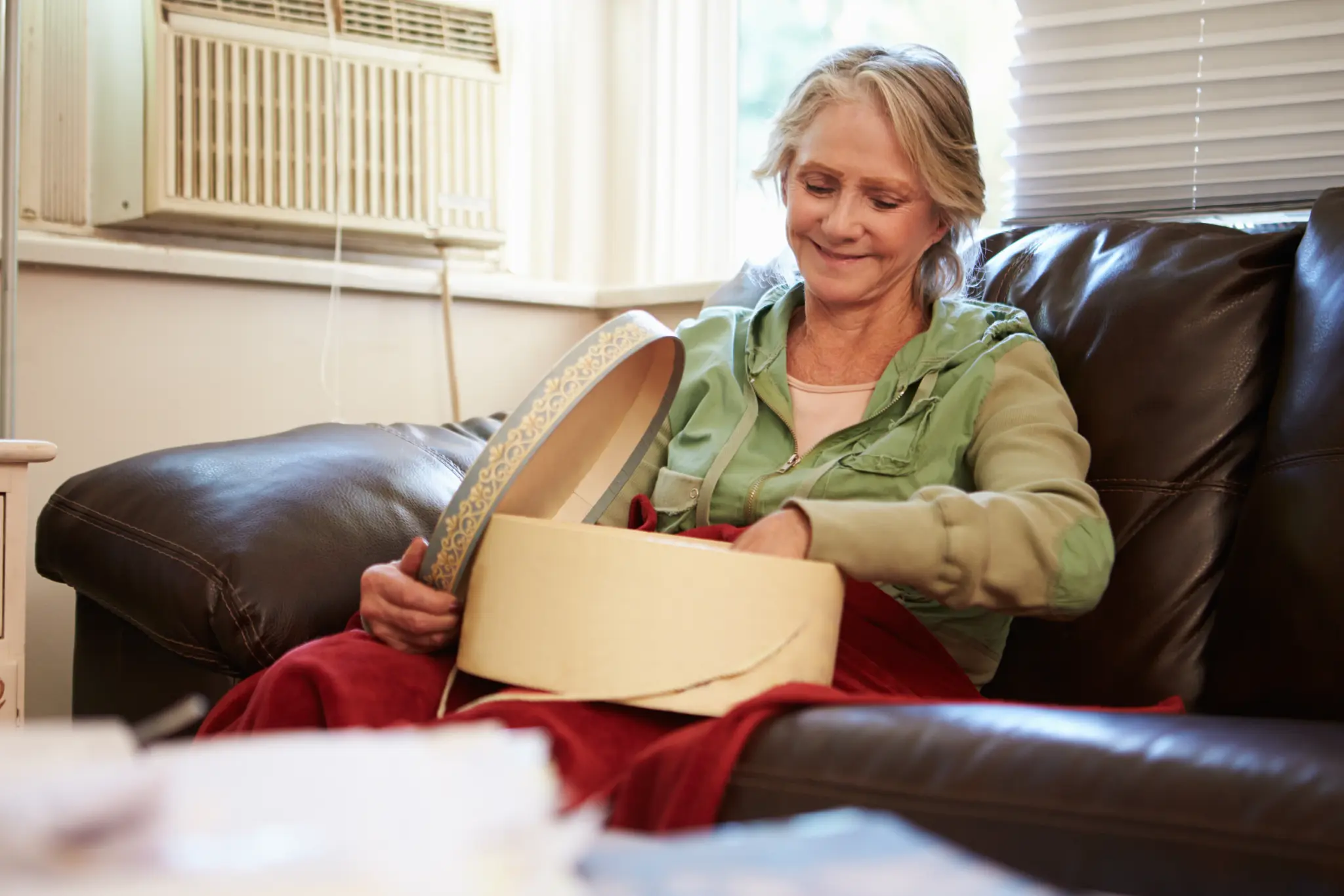 Image of a woman, seated in an armchair and smiling as she sorts through a box on her lap.