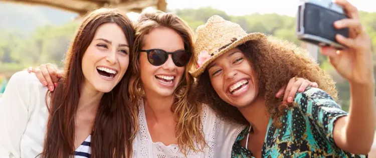 Photo of three women with their arms around one another as they lean in to take a selfie