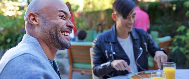 Two men at restaurant table eating. Both men are smiling and laughing.