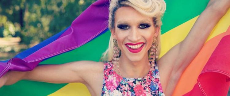 LGBTQ+ person holding up a rainbow pride flag and smiling