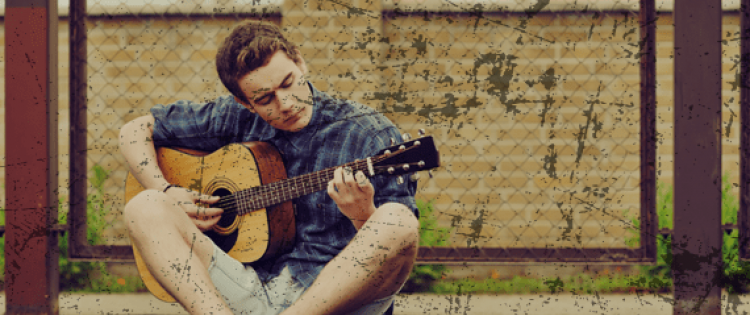 Young man sitting with legs crossed and playing guitar outside