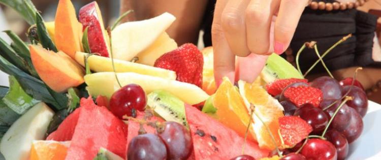Photo of a woman's hand picking a strawberry off of a large platter with a wide variety of fruit.