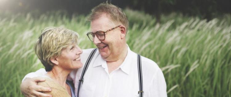 Photo of a couple standing together in a field smiling at one another, a man with his arm around the woman