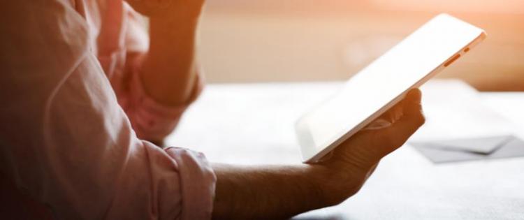 Photo of a man sitting at a table, studying a tablet computer.