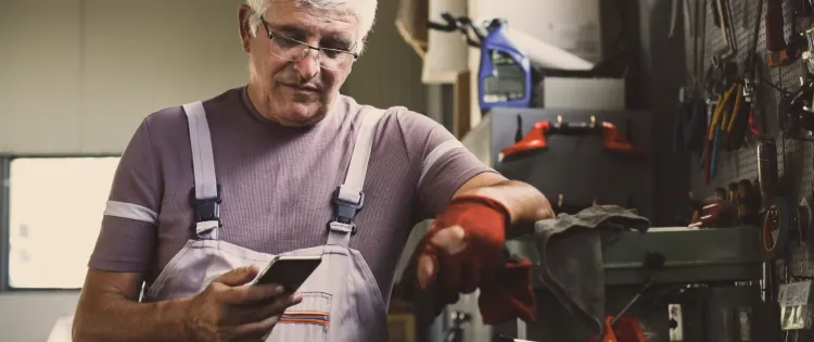 Image of a man consulting his phone while taking a break in his workshop.