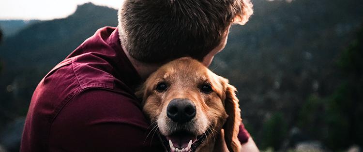 A man hugging his smiling dog outdoors.