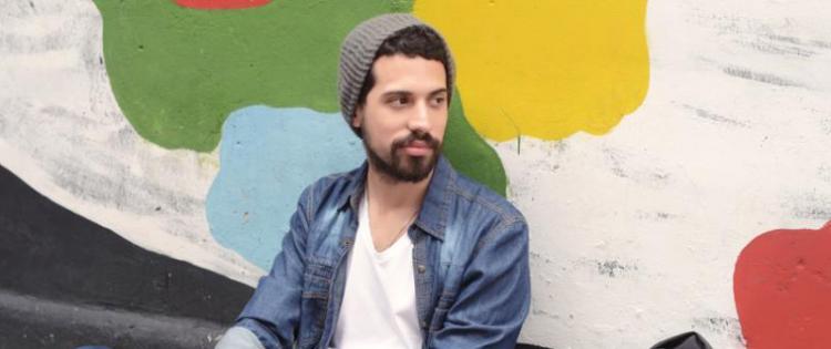 Photo of a man sitting on the ground, leaning against a wall painted with a colorful mural.