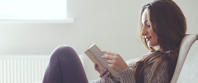 A woman reading a book on the couch.