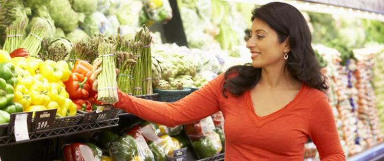 Photo of a woman picking out asparagus while standing behind her shopping cart.