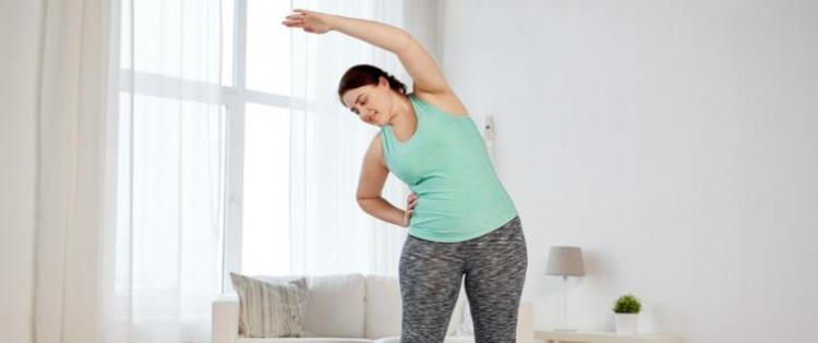 Photo of a woman stretching to the side while standing on a yoga mat.