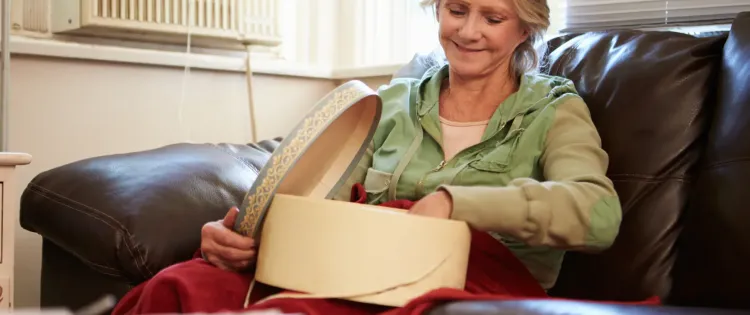 Image of a woman, seated in an armchair and smiling as she sorts through a box on her lap.