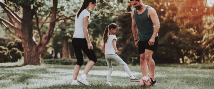 Photo of a happy young family playing soccer in a park.