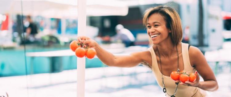 Photo of a woman holding tomatoes she's selected at a farmer's market.