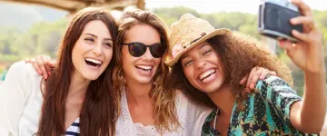 Photo of three women with their arms around one another as they lean in to take a selfie