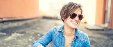 Photo of a woman wearing aviator sunglasses. She's sitting in an alley.