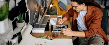 Image of a person seated at a desk making art on a graphics tablet.