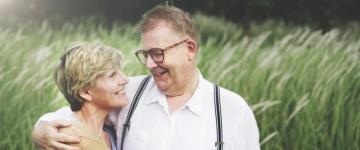 Photo of a couple standing together in a field smiling at one another, a man with his arm around the woman