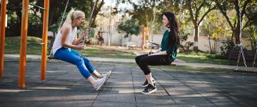 Two women sitting on swings, facing each other.