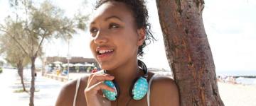 Photo of a smiling young woman leaning against a tree. She has polka dot headphones around her neck.