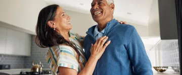 Image of an older couple in a kitchen, smiling and enjoying a celebratory embrace.