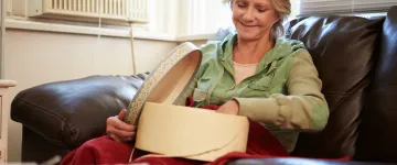 Image of a woman, seated in an armchair and smiling as she sorts through a box on her lap.
