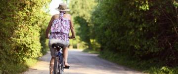 Photo of a woman riding her bike down a paved, tree-lined road.