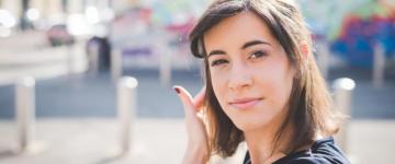 Photo of a young woman looking at the camera, tucking her hair behind her ear.