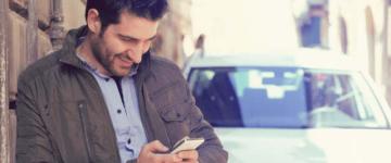 Man leaning against wall and looking at mobile phone.