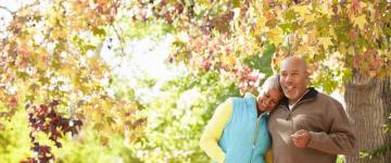 Photo of a couple walking under autumn leaves, the woman rests her head on the man's shoulder