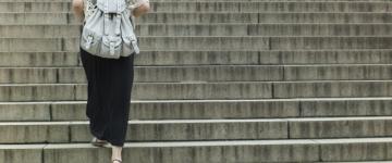 Photo of a woman in a skirt, wearing a backpack and walking away from the camera up a flight of concrete stairs