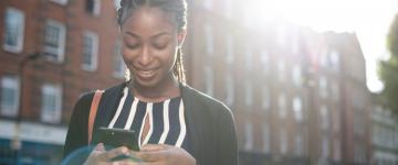 Woman in city looking down at phone and smiling