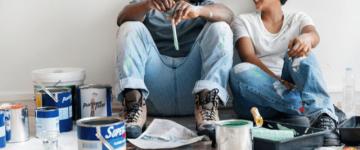 Photo of a young couple resting on the floor surrounded by painting supplies