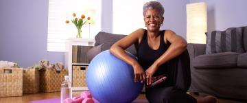 Photo of a woman in her home with water, an exercise ball, yoga mat, and light weights
