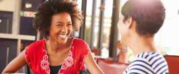 A photo of two women sit drinking coffee, smiling, and talking