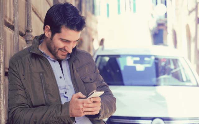 Man leaning against wall and looking at mobile phone.