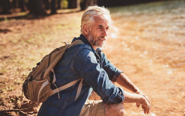 Photo of a man with a backpack, sitting by a forest stream to rest