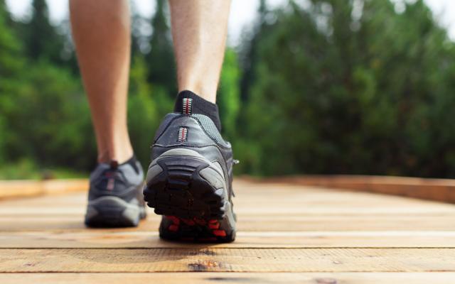 Photo of a pair of feet in tennis shoes walking across a wooden bridge with trees in the distance