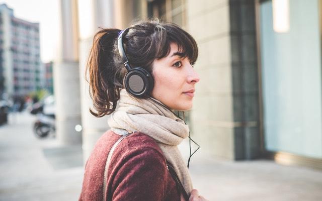 Photo of a woman walking down a city street with headphones and a scarf looks back over her shoulder