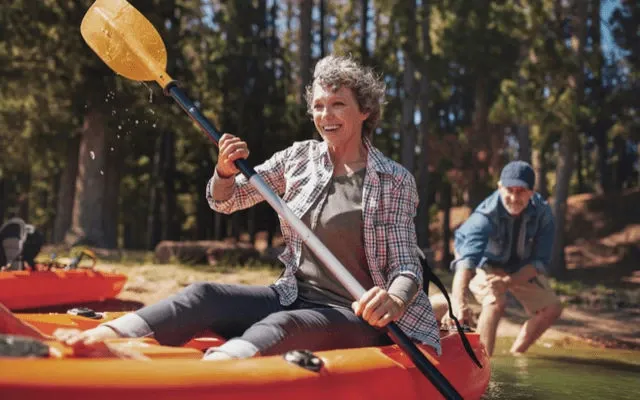 Photo of an older woman in a kayak getting pushed from shore by her husband